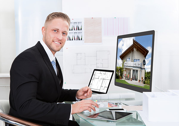 Businessman or estate agent checking a property portfolio online while sitting at his desk in the office looking at the exterior of a rural house visible on the desktop monitor