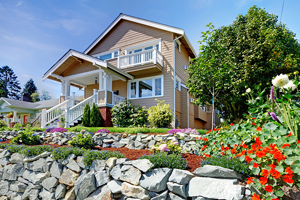 Two story beige nice house on the rocky hill with flowers.